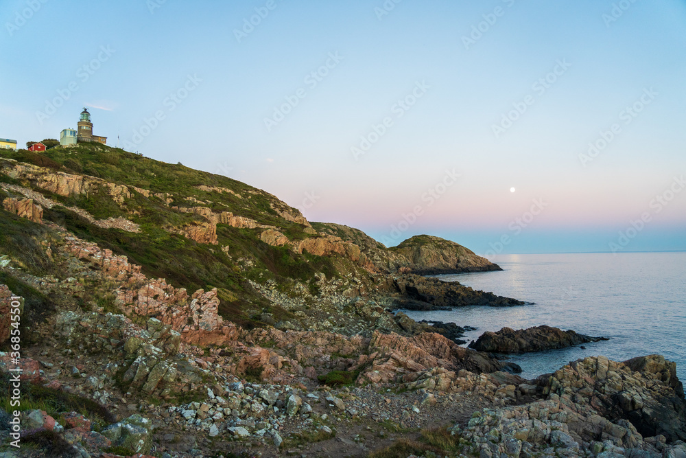 Lighthouse with full moon after sunset during summer season at Kullaberg nature reserve in south Sweden. Selective focus.