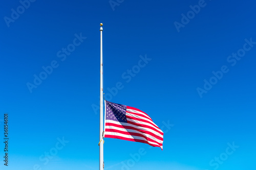 Fotografija Flag of the United States flying at half staff waving in the wind under blue sky