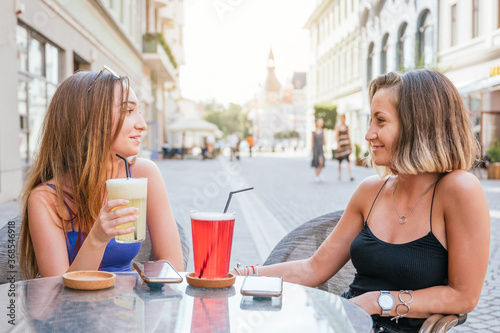 Two female friends talking, drinking lemonade and having fun in a restaurant