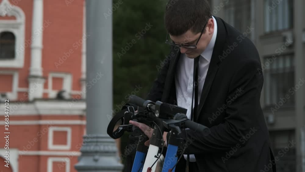 Businessman is using city technology and is about to rent an electric scooter using wireless technology. Scooter sharing. Rack focus. Businessman is using city technology and is about to rent an electric scooter using wireless technology. Scooter sharing. Rack focus.