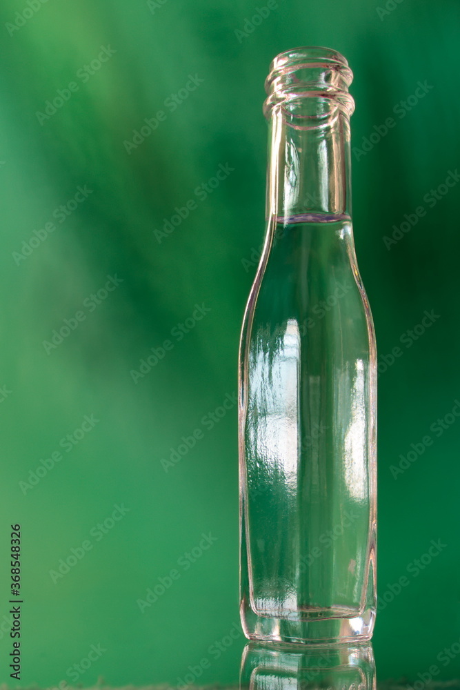 glass bottle filled with a transparent liquid on a shiny surface and a green background with stains. glass bottle filled with a transparent liquid on a shiny surface and a green background with stains.