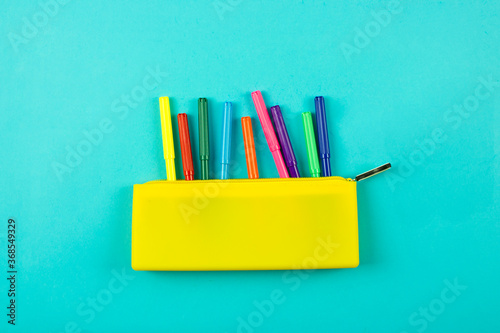 yellow pencil case and a set of bright colored markers for drawing and coloring on a blue background. Color palette.