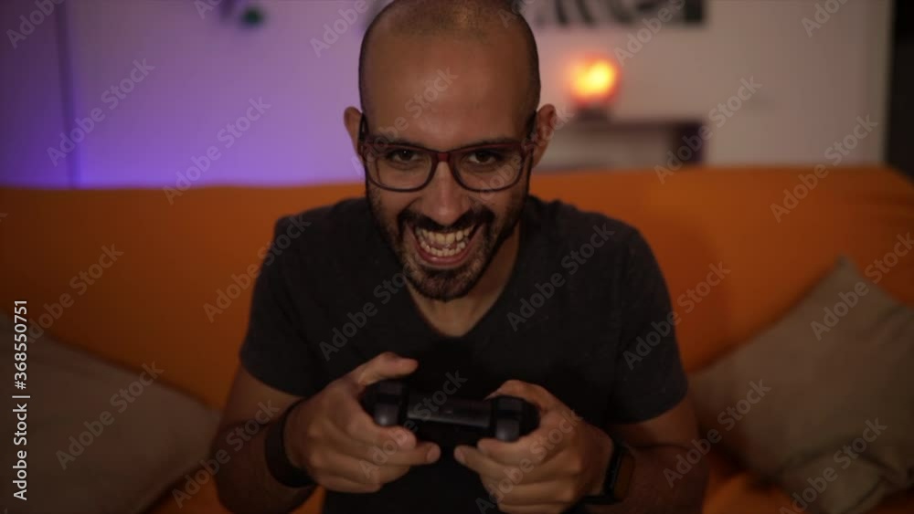 Slow Motion: smiling attractive man plays a video game on the sofa having fun. Winner sign with his arm. Caucasian man plays video game late at night Slow Motion: smiling attractive man plays a video game on the sofa having fun. Winner sign with his arm. Caucasian man plays video game late at night