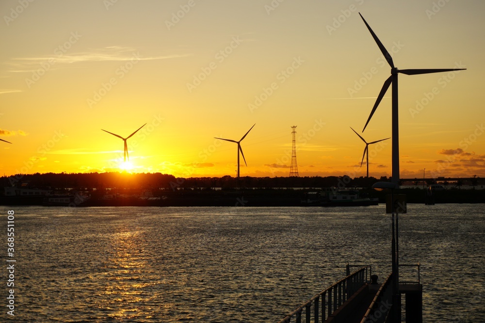 Beautiful sunset at jetty over the water with windmills and industrial shipping.
