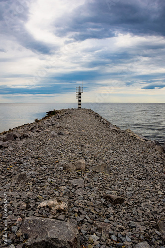 Lighthouse on a stone spit against the backdrop of a bright blue sky