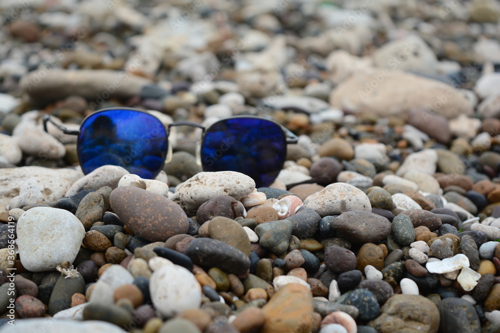Lentes de sol azules sobre playa de piedritas marrones Lentes de sol azules sobre playa de piedritas marrones