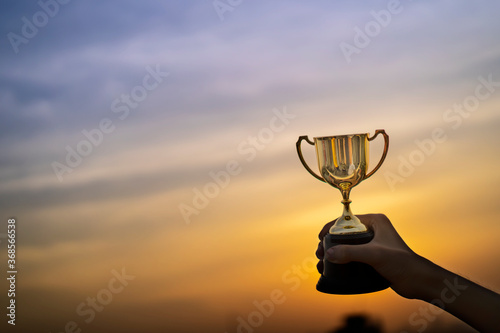 Business hold a trophy showing success until receiving the award. Champion golden trophy for winner  Evening sky background