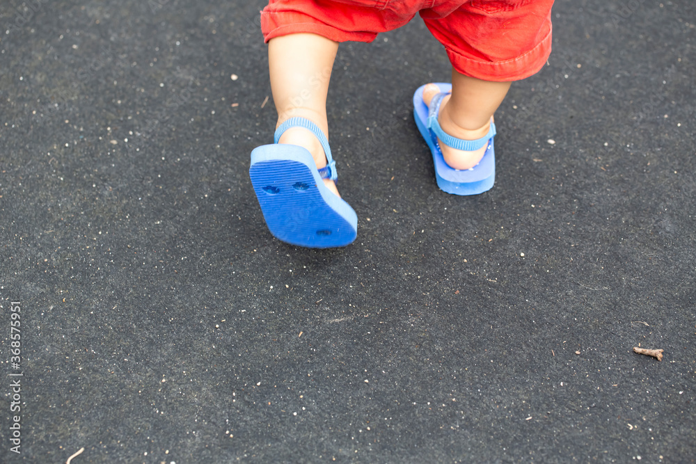 歩いている子供の足と青いビーチサンダルと黒バックとコピースペース
