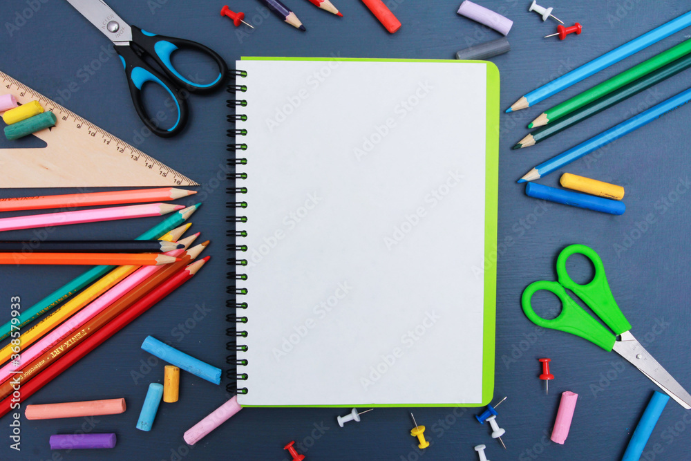 White page of notebook with pencils, copy space for text. Copybook, scissors, ruler, office supplies on dark blue background. Top view, flat lay. Back to school in autumn concept White page of notebook with pencils, copy space for text. Copybook, scissors, ruler, office supplies on dark blue background. Top view, flat lay. Back to school in autumn concept