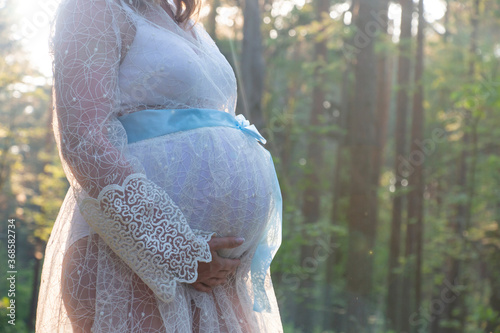 A pregnant woman in a dress holds her hands on her stomach. The concept of pregnancy, motherhood, preparation and expectation. Close-up, copy space Beautiful tender mood photo of pregnancy