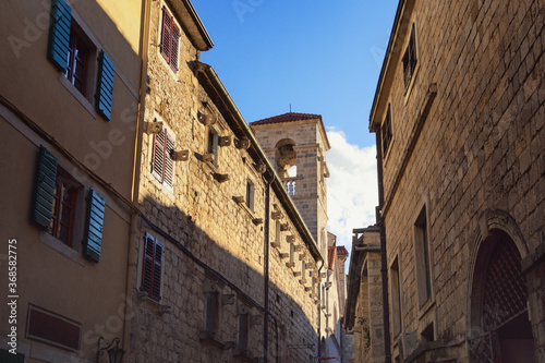 Light and shadow, narrow street of ancient Mediterranean town on sunny winter day. Montenegro. Old Town of Kotor, UNESCO-World Heritage Site. View of St. Francis Monastery Tower