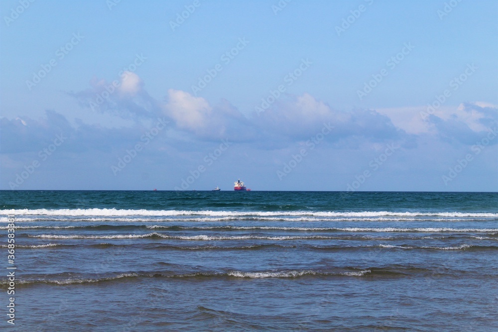 Playa con oleaje suave y algunos barcos a lejos