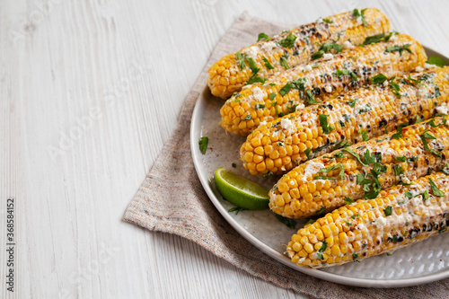 Homemade Elote Mexican Street Corn on a plate on a white wooden background, side view. Copy space.