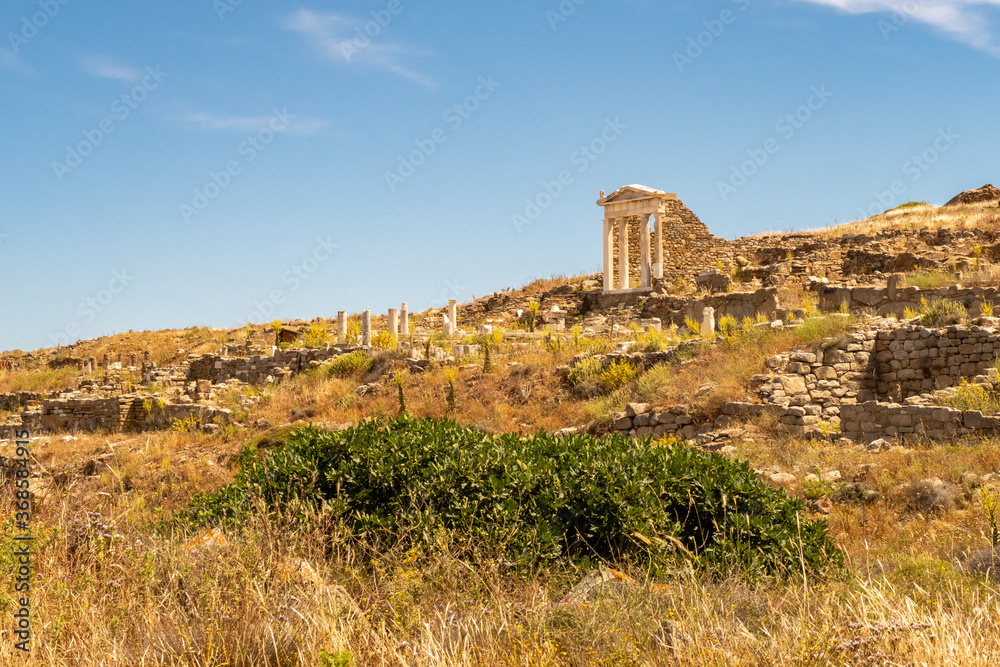 Well preserved Temple of Isis on Delos Island located on the hill above the ancient city with other ruins and blue sky in the background, Greece. 