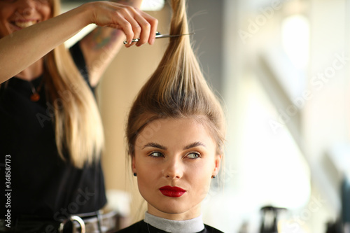 Young Woman with Ponytail Getting Haircut in Salon. Hairdresser Cutting Female Hair with Scissors. Professional Haircut for Young Blonde Girl Client in Beauty Studio. Head and Shoulders Photography