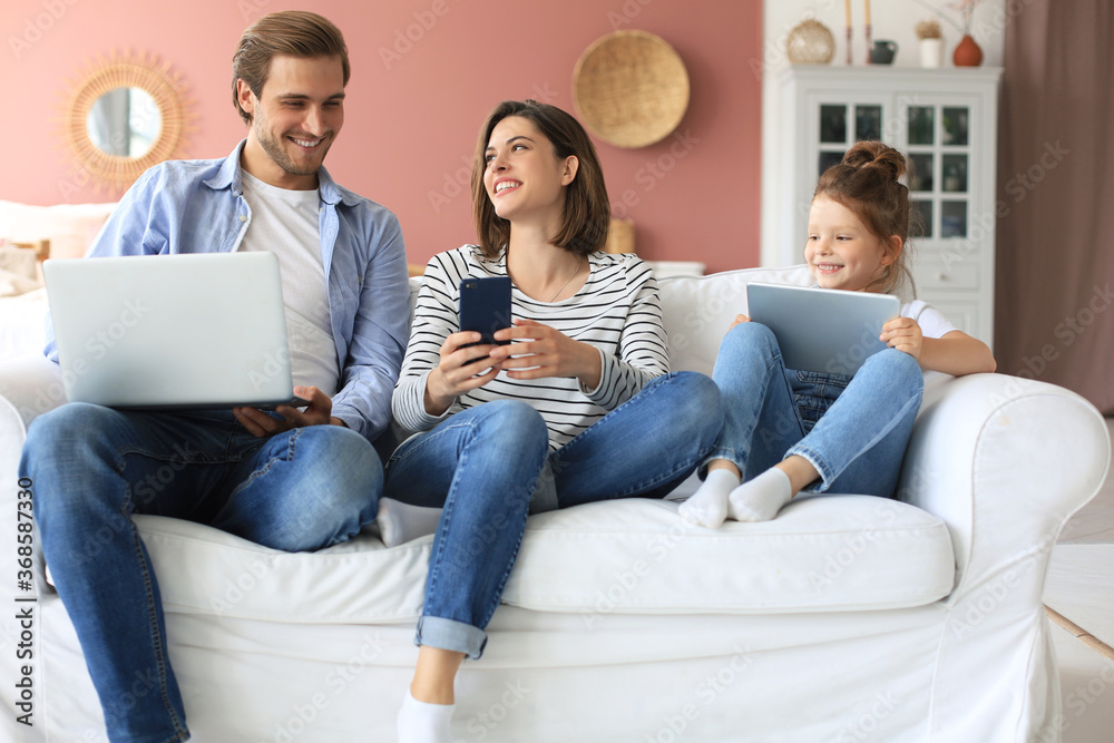 Father, mother and daughter using electronic devices sitting on sofa at living room. Father, mother and daughter using electronic devices sitting on sofa at living room.