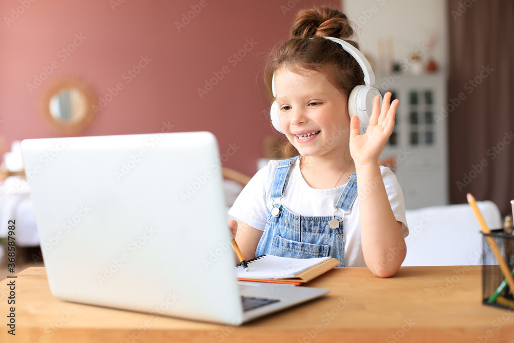Distance learning. Cheerful little girl girl in headphones using laptop studying through online e-learning system. Distance learning. Cheerful little girl girl in headphones using laptop studying through online e-learning system.