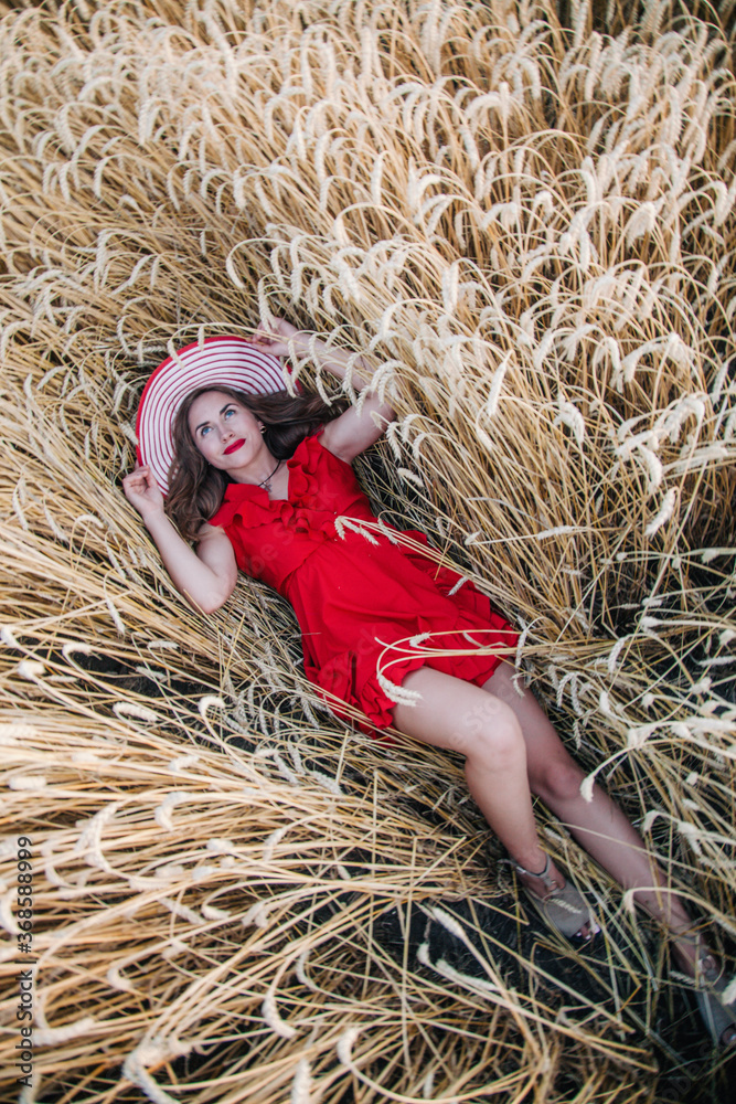 Beautiful girl in red dress and striped hat posing in a wheat field Beautiful girl in red dress and striped hat posing in a wheat field