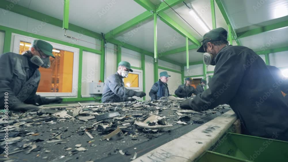 Recycling center workers sort trash on a conveyor.