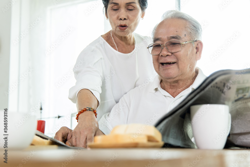 An Asian elderly couple reading a newspaper.