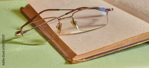 The glasses are lying on an open book on a solid background