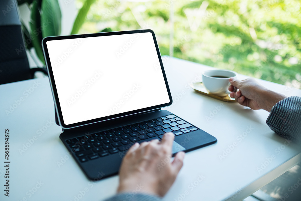 Mockup image of a woman touching on tablet touchpad with blank white desktop screen as computer pc while drinking coffee