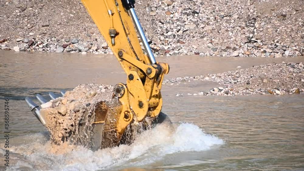 Excavator bucket close up. Excavator digging river rocks sand and pebbles. Heavy industry and environment. Ecological disaster. Machine dredging river canal. Dam building. Slow motion, static shot