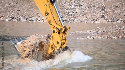 Excavator bucket close up. Excavator digging river rocks sand and pebbles. Heavy industry and environment. Ecological disaster. Machine dredging river canal. Dam building. Slow motion, static shot photo