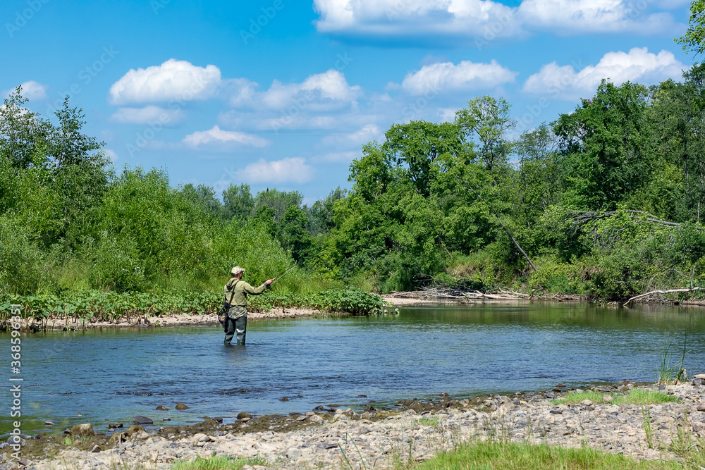 A man is fishing with fly fishing in the river on a summer day.