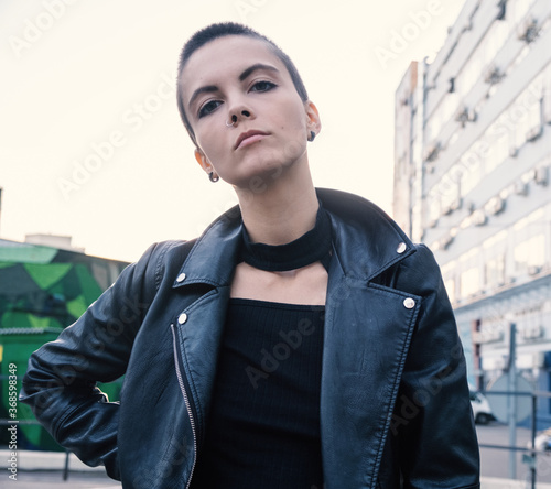 Fotografie Serious rebel informal teenage girl with bald hair and piercing in urban outdoor city background
