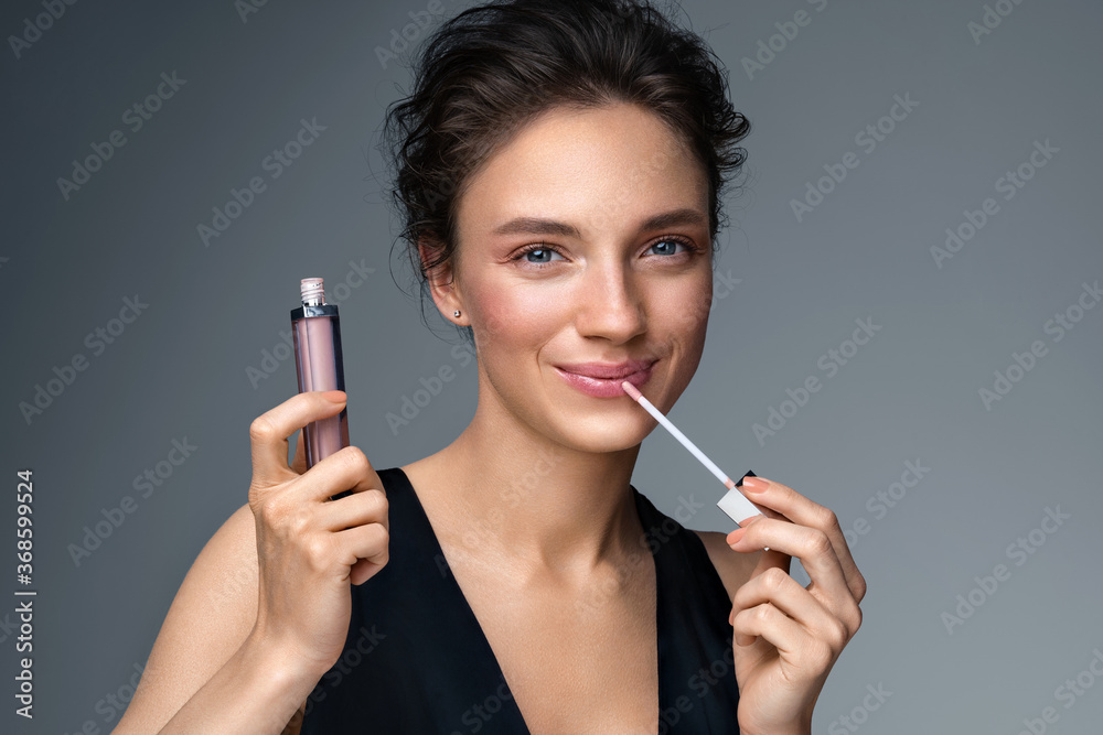 Obraz premium Woman with lip gloss. Photo of woman with perfect makeup on gray background. Beauty concept