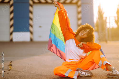 Beautiful African American lesbian girl with LGBT rainbow flag at sunset. Young curly hair woman posing with lgbt pride flag.