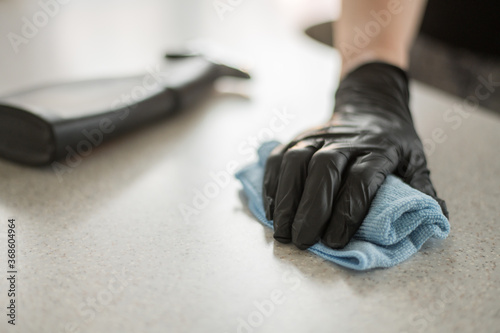 A hand in black gloves holds a microfiber cleaning cloth and a spray with sterilizing make disinfection for good hygiene