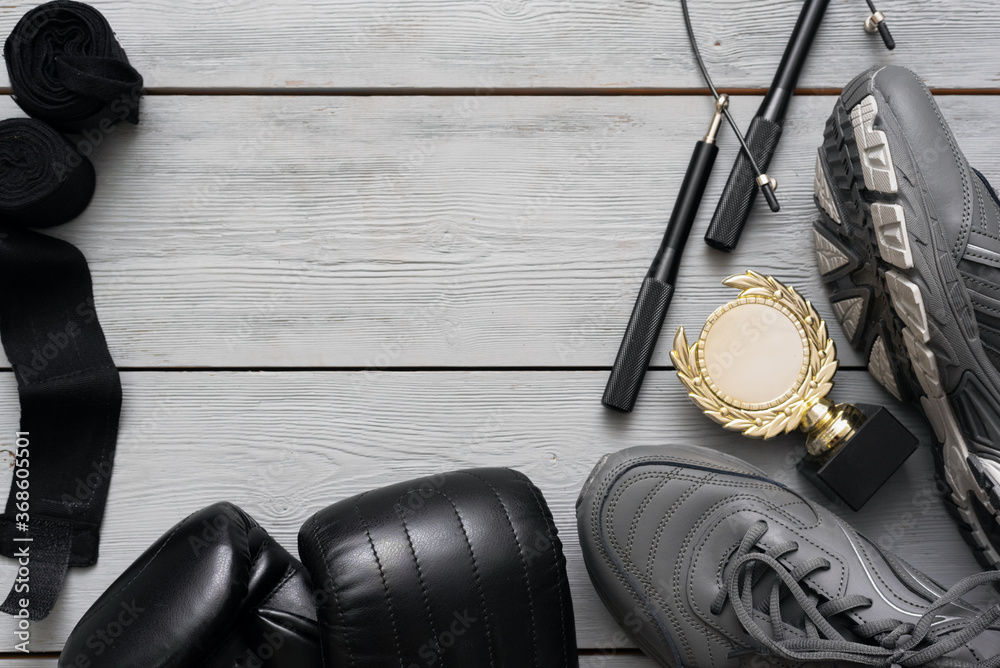 Boxing gloves, sneakers, jumping rope and golden award trophy on the wooden floor flat lay background with copy space.