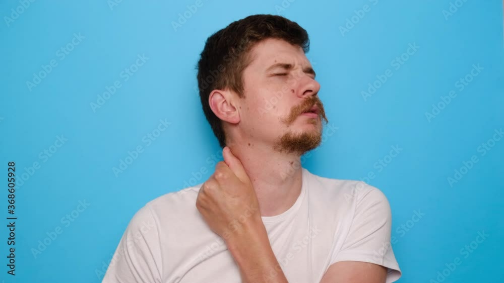 Upset young man massaging hurt stiff neck, fatigued sad millennial guy rubbing tensed muscles to relieve joint shoulder pain, wears t-shirt, isolated on blue studio background. Fibromyalgia concept Upset young man massaging hurt stiff neck, fatigued sad millennial guy rubbing tensed muscles to relieve joint shoulder pain, wears t-shirt, isolated on blue studio background. Fibromyalgia concept