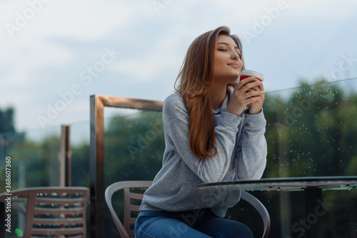 Cheerful loving girl enjoying coffee break looking away while sitting outdoor at terrace. City style