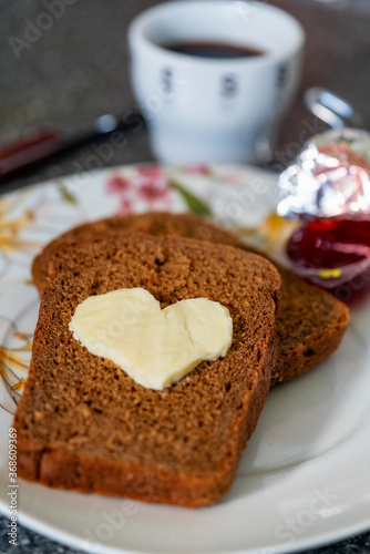 Heart shaped butter with jam on a slice of bread next to a cup of coffee