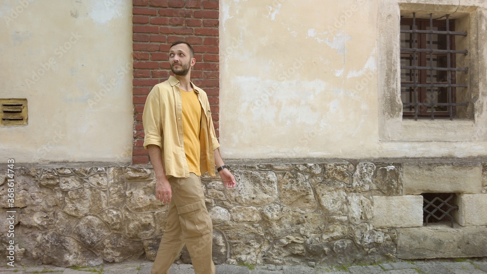 Side view of adult male traveler in yellow shirt walks along a narrow old street. Tourism during quarantine
