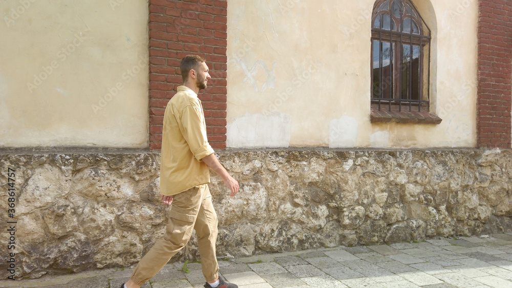 Side view of adult male traveler in yellow shirt walks along a narrow old street. Tourism during quarantine