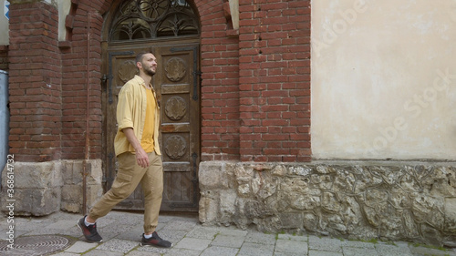 Side view of adult male traveler in yellow shirt walks along a narrow old street. Tourism during quarantine © Honchar