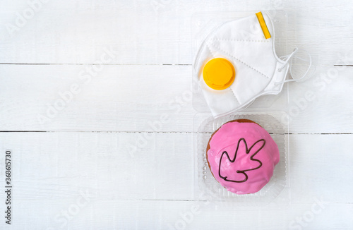 Pandemic concept, coronavirus infection outbreak, food delivery for healthcare workers. Berliner donut in a container and a medical mask on a white background. Copy space. photo