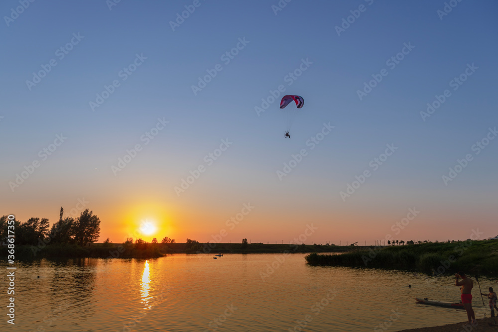 Naklejka premium paraglider at sunset over the lake