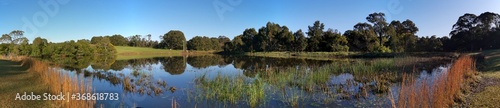 Fototapeta Naklejka Na Ścianę i Meble -  Beautiful morning panoramic view of a peaceful pond in a park with reflections of deep blue sky and tall trees, Fagan park, Galston, Sydney, New South Wales, Australia