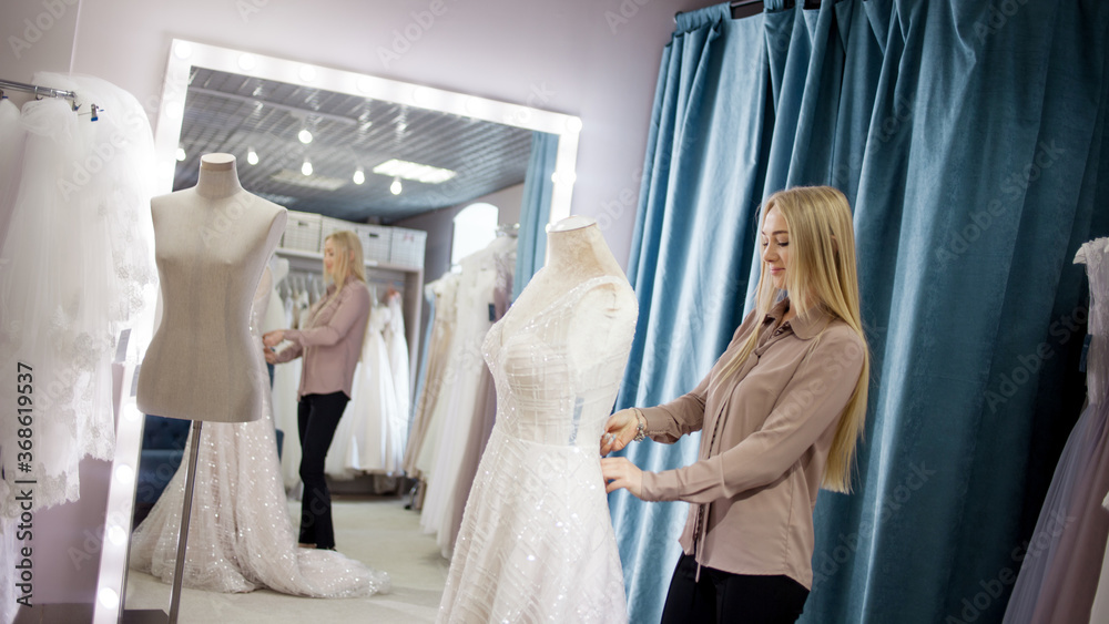 hostess of the wedding salon looks at the wedding dress. Small business, hostess of the wedding salon looks at the wedding dress. Small business,