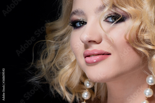 Gorgeous blonde, portrait on a black background. Beautiful young girl, makeup for the celebration.