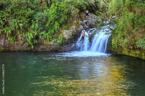 Raparapahoe Falls in the Bay of Plenty  New Zealand  cascading into a pool surrounded by native forest. Two men are climbing up the waterfall with the help of a rope