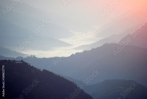 Mist and clouds hover around the various hills connected mountain valley below as seen from Sombaria during sunrise in West Sikkim, India.