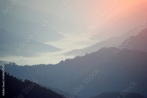 Mist and clouds hover around the various hills connected mountain valley below as seen from Sombaria during sunrise in West Sikkim, India.