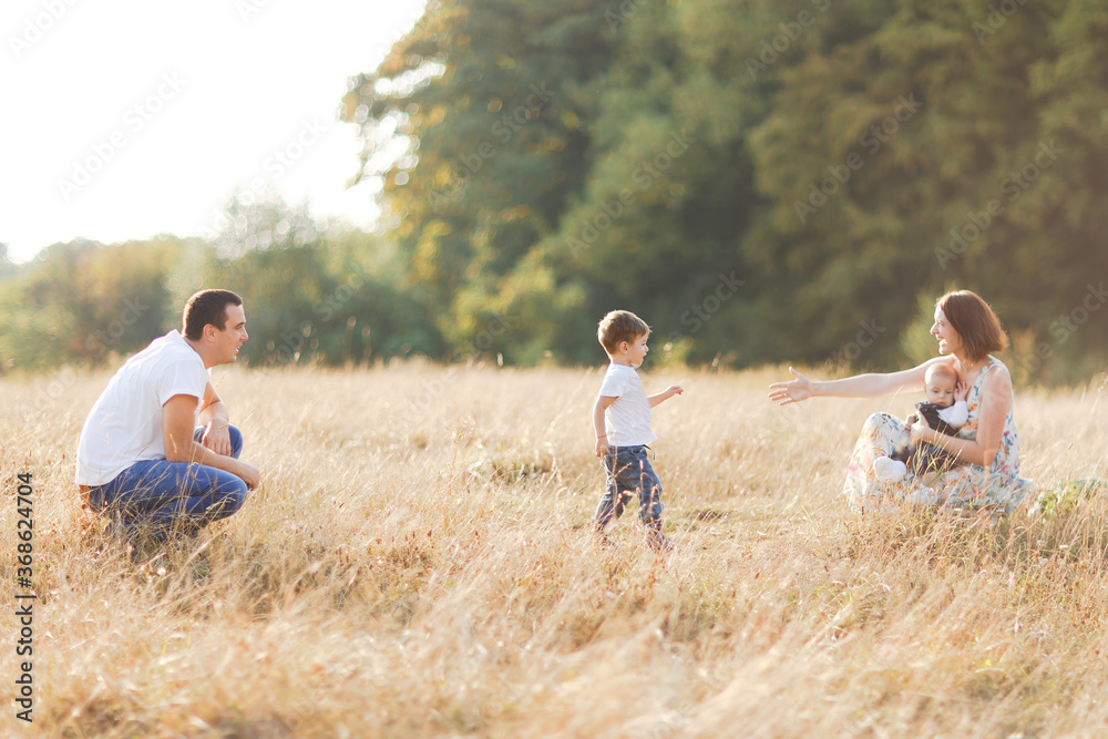 Family with children walking outdoors in summer field at sunset. Father, mother and two children sons having fun in summer field. People, family day and lifestyle concept