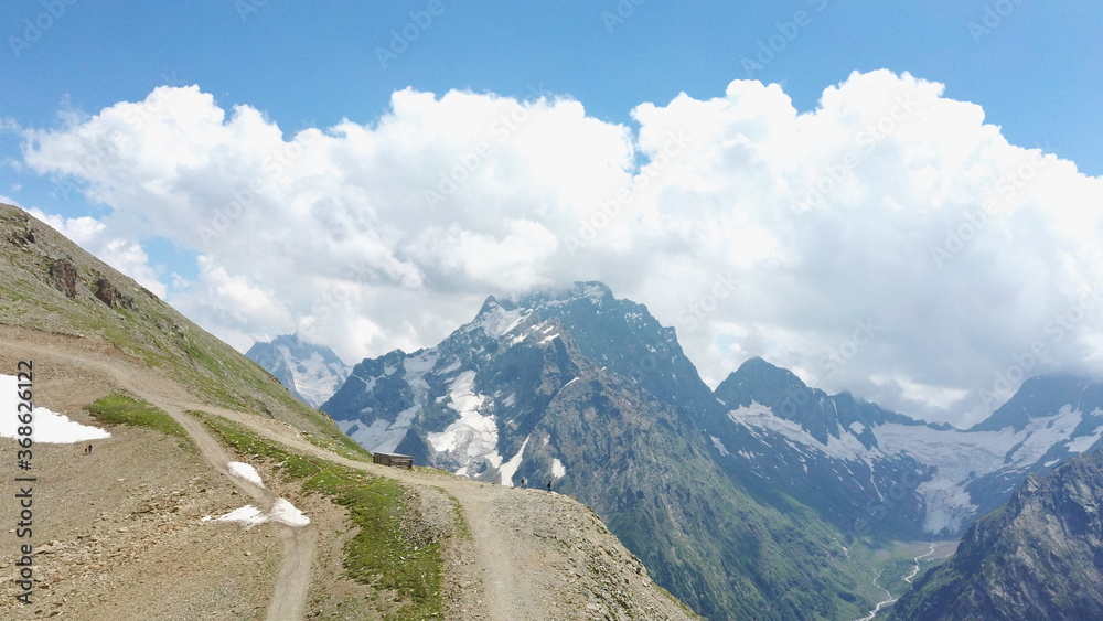 Snowy mountain against cloudy sky. From below white clouds floating on blue sky over mountain ridge covered with snow on sunny day in nature Snowy mountain against cloudy sky. From below white clouds floating on blue sky over mountain ridge covered with snow on sunny day in nature